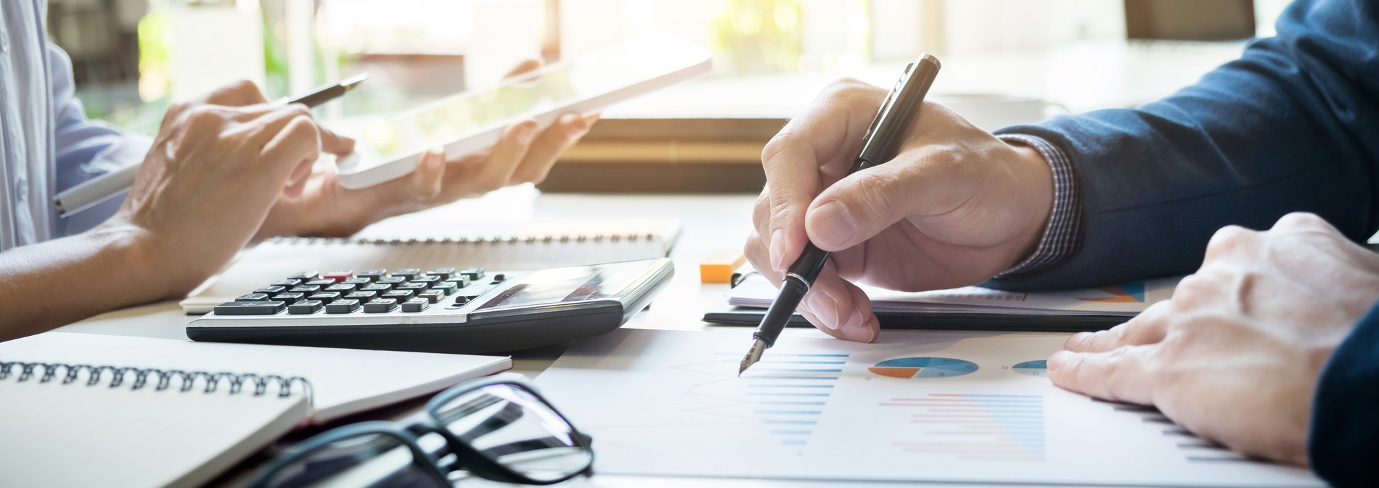Hands engaged in a business discussion with a calculator, notebooks, and charts on a table